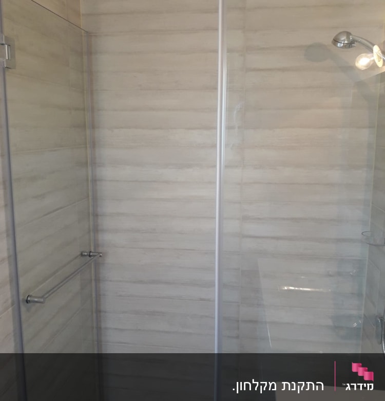 מקלחון זכוכית עם ראש מקלחת מתכתי על קיר